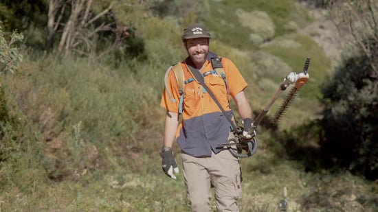 A worker in safety gear carrying a hedge trimmer working on vegetation management in the ski area